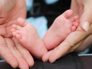 Woman holding a baby&rsquo;s feet; image by Bonnie Kittle, via Unsplash.com.