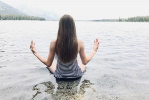 Woman in seated meditation in the water at a lakeshore; image by Audrey Hope, via Reshot.com.