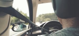 Rear shot of man in driver&rsquo;s seat of car, driving down the road; image by Milan de Clercq, via Unsplash.com.