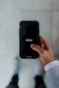 Man with black smartphone with &ldquo;Uber&rdquo; on the screen; image by Austin Distel, via Unsplash.com