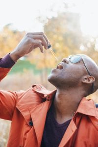 Colorado man taking a dose of hemp extract oil outside; image by R+R Medicinals, via Unsplash.com.