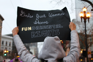 Person in grey hoodie holding sign saying, &ldquo;Girls Just Wanna Have FUNdamental Rights&rdquo;; image by Lucia, via Unsplash.com.