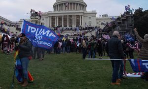 People milling around in front of the Capitol building, some carrying signs.