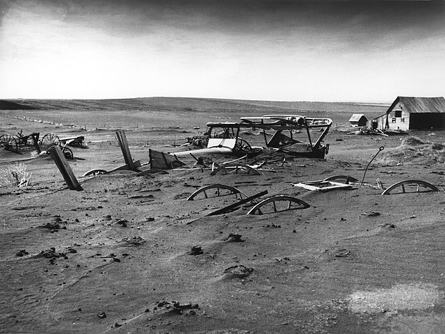 Vintage 1936 photo of Dust Bowl ruination, farm equipment nearly buried under sediment.