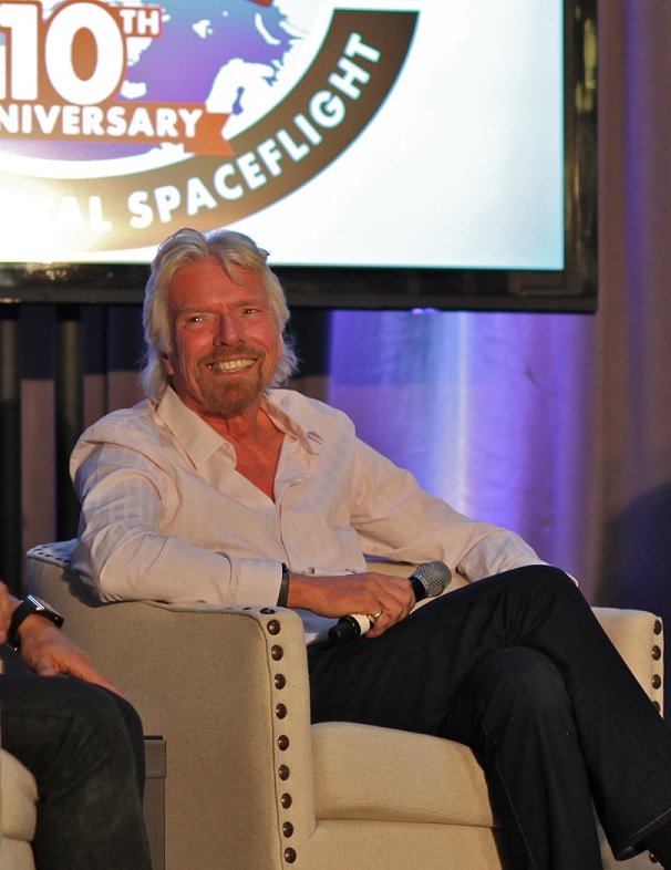 A seated blond man in a shirt unbuttoned to the chest, smiles.