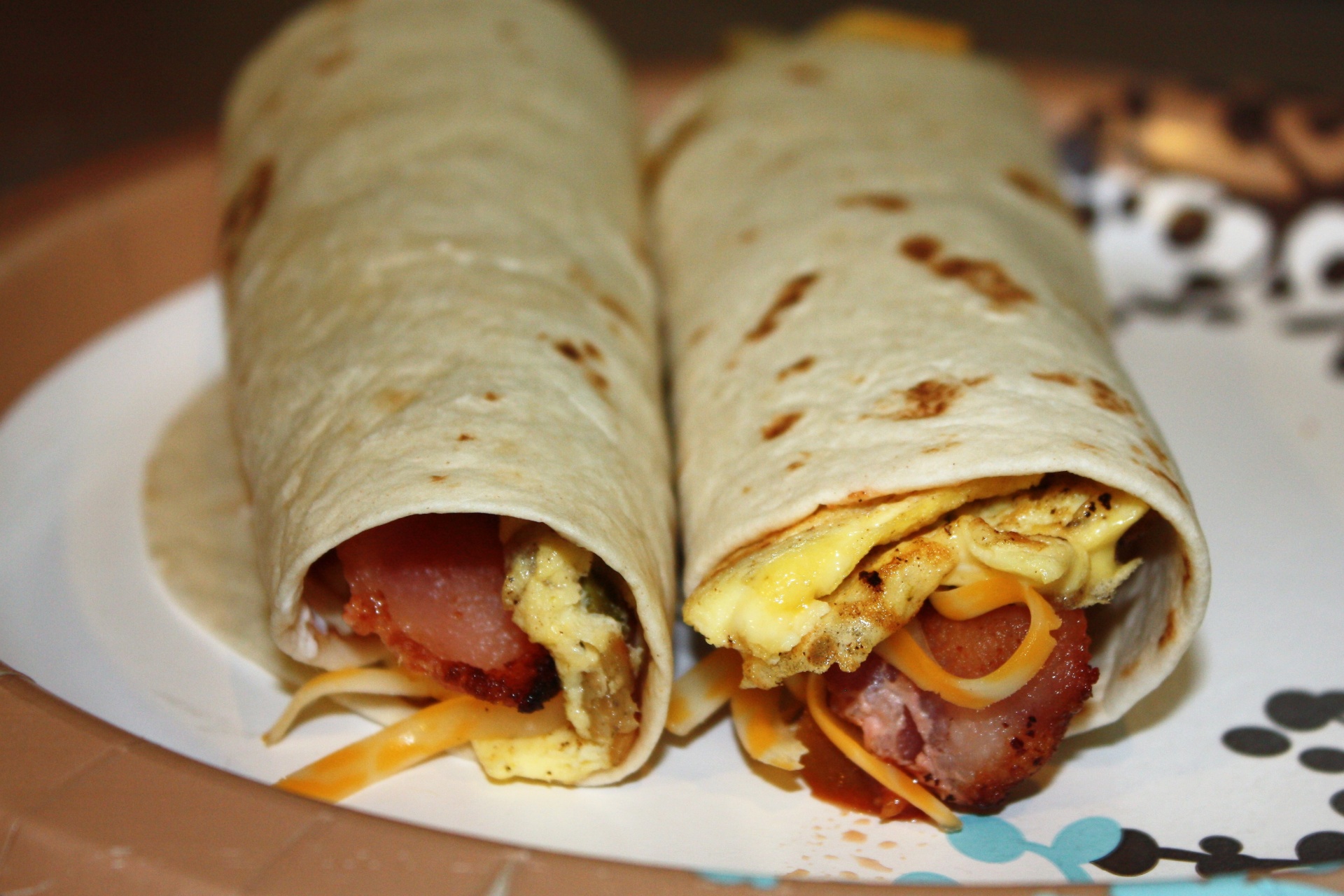 Two egg and meat filled breakfast burritos on a plate.