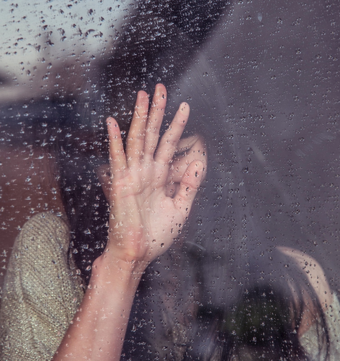 Woman resting her hand on a rain-soaked window; image by Milada Vigerova, via Unsplash.com.