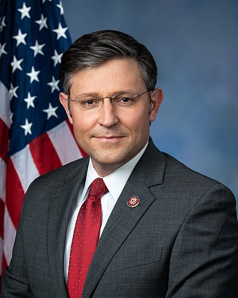 Standard portrait of a man in a suit and tie backed by the American flag.