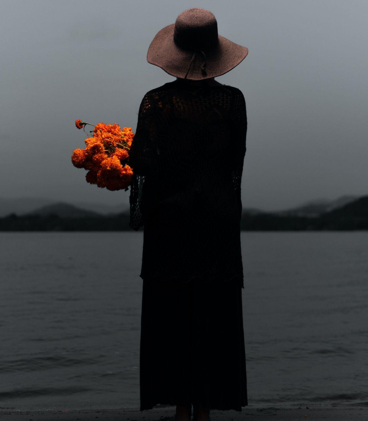 Woman on beach with flowers; image by Oscar Mill&agrave;n, via Pexels.com.
