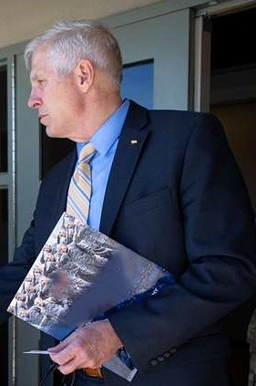 An older man with short hair in a suit looks to the left.
