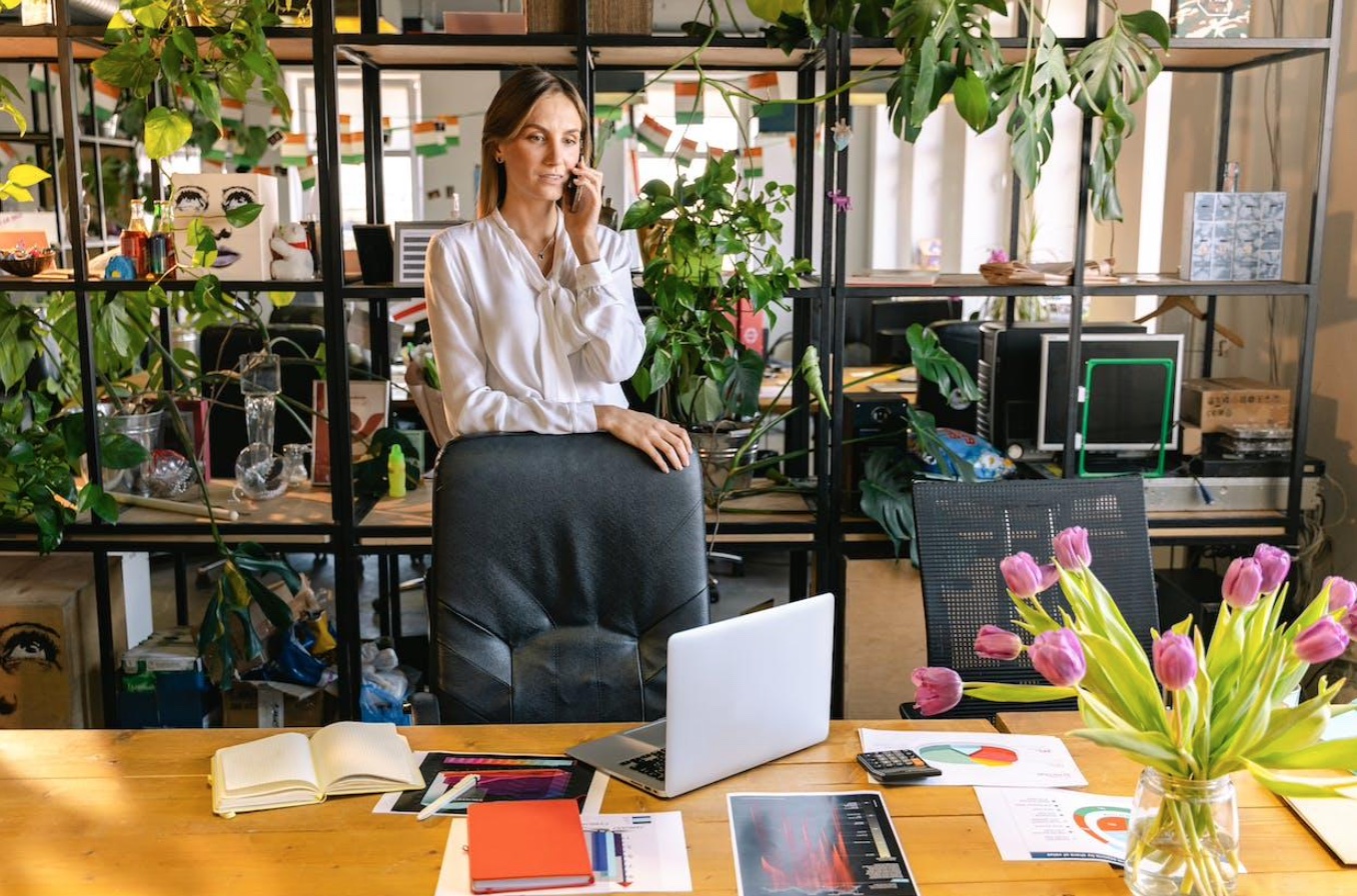 Woman in office talking on phone, plants in background; image by Antoni Shkraba, via Pexels.com.