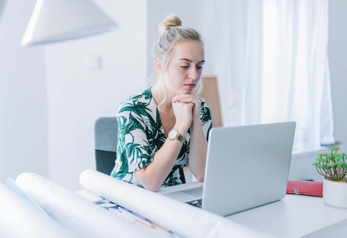 Woman at desk in office working on laptop; image by Freepik, via Freepik.com.